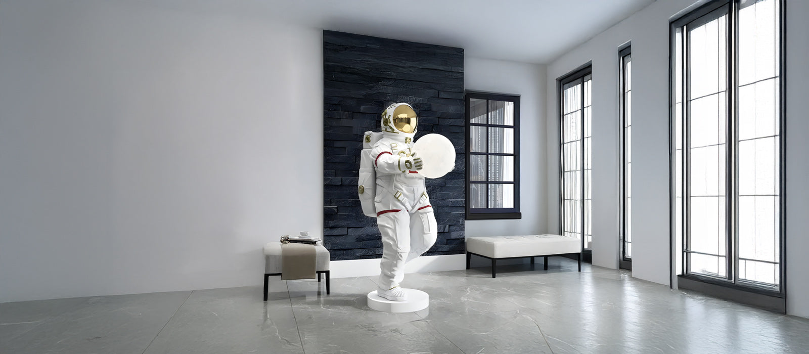 A sculpture of an astronaut with a reflective gold visor is displayed in a modern room with gray walls and large windows. Nearby are a white bench and a small table with a coffee cup.