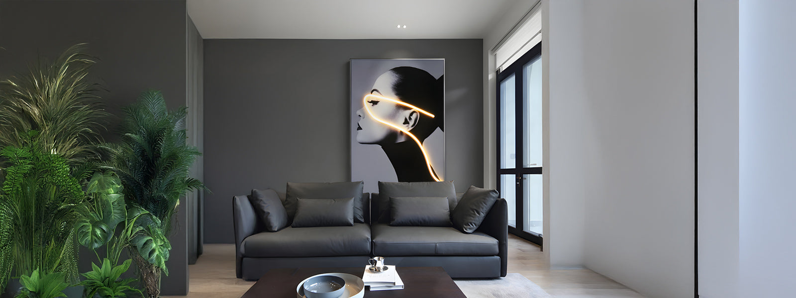 A modern living room with a dark gray sofa, large artwork featuring a face with neon lines, potted plants, and a dark coffee table. Soft lighting and large windows create a spacious and elegant atmosphere.