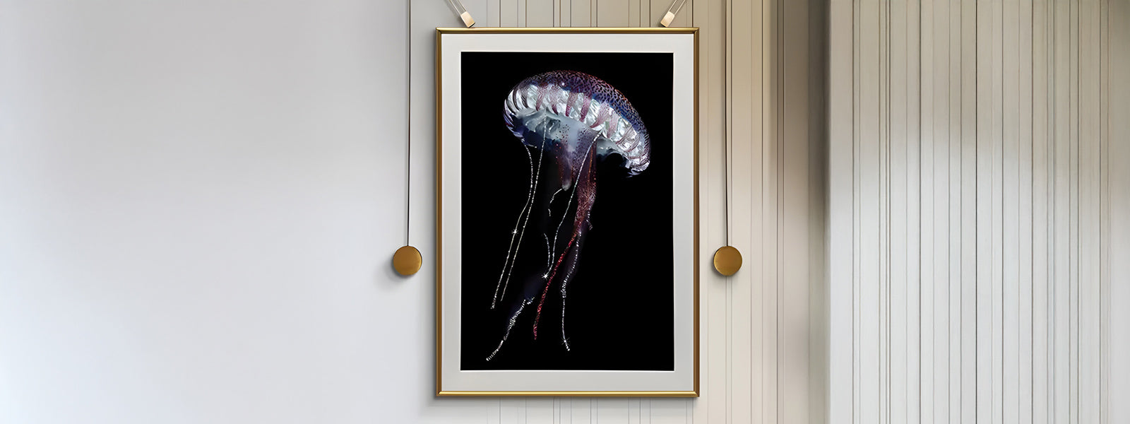 A jellyfish art piece in a gold frame is displayed on a striped wall. The jellyfish has a translucent body with long, flowing tentacles against a black background.