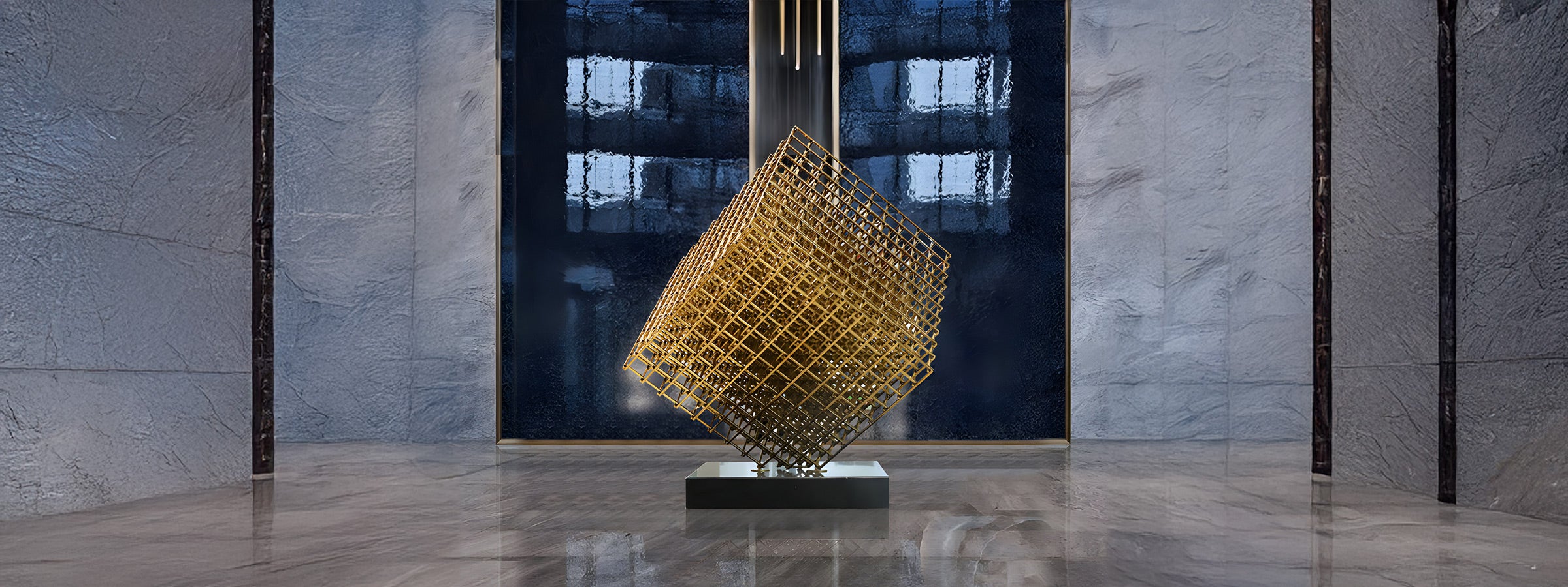 Gold geometric cube sculpture made of intersecting metal bars, positioned on a black base in the center of a modern interior with stone walls and reflective marble flooring.