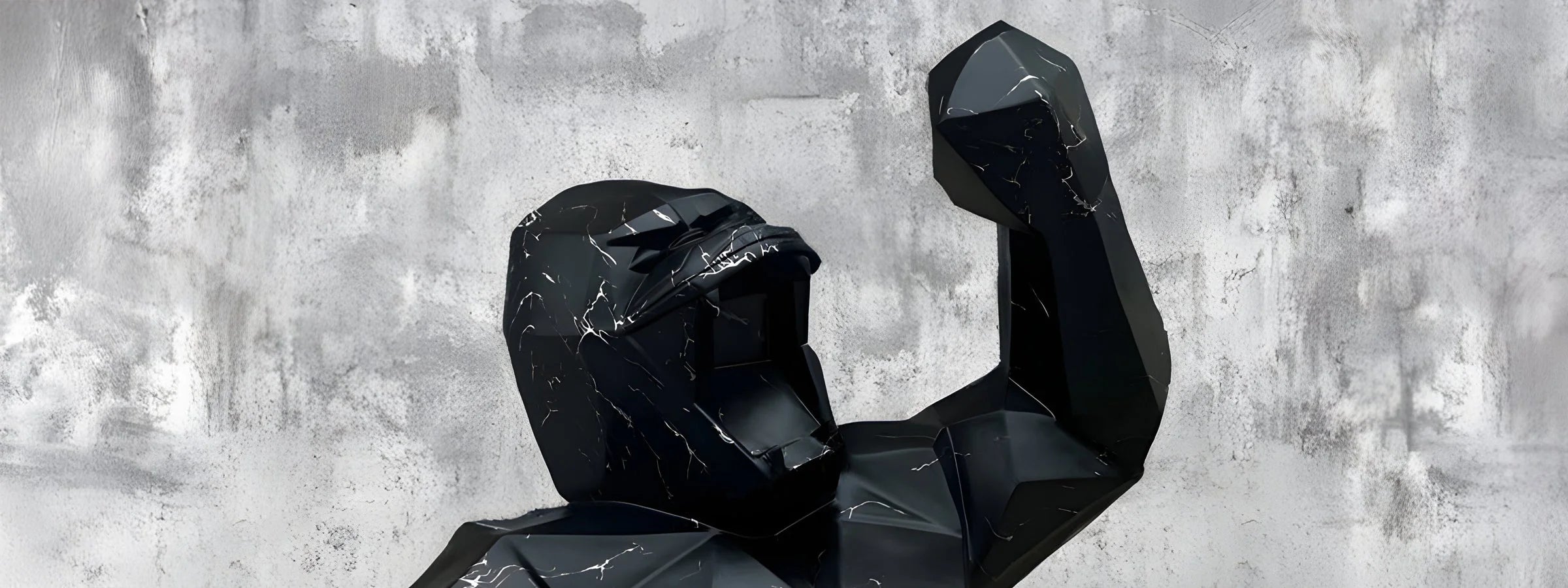 Black geometric gorilla sculpture with angular, faceted surfaces and marbled texture. The gorilla is posed with raised fists against a gray concrete wall, featuring sharp edges and a matte finish, conveying strength and movement.