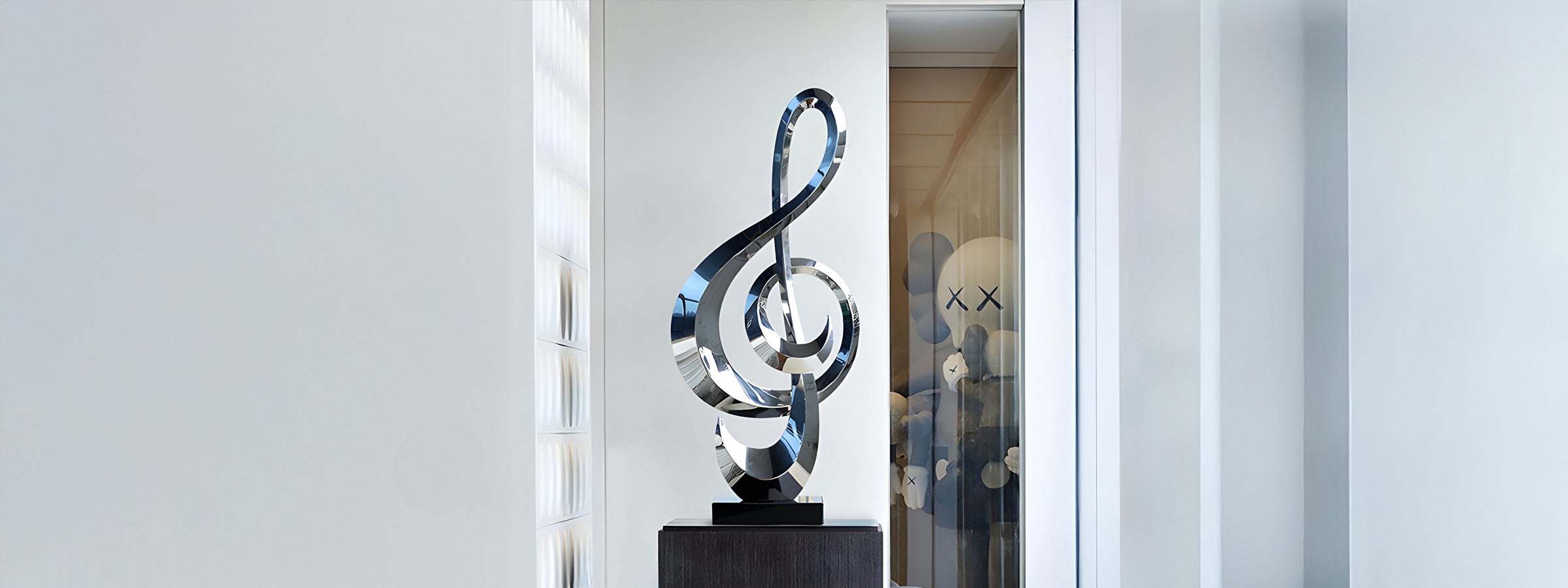 Polished stainless steel sculpture featuring an abstract treble clef design, displayed on a black pedestal in a modern indoor setting with a glass partition and minimalist decor.