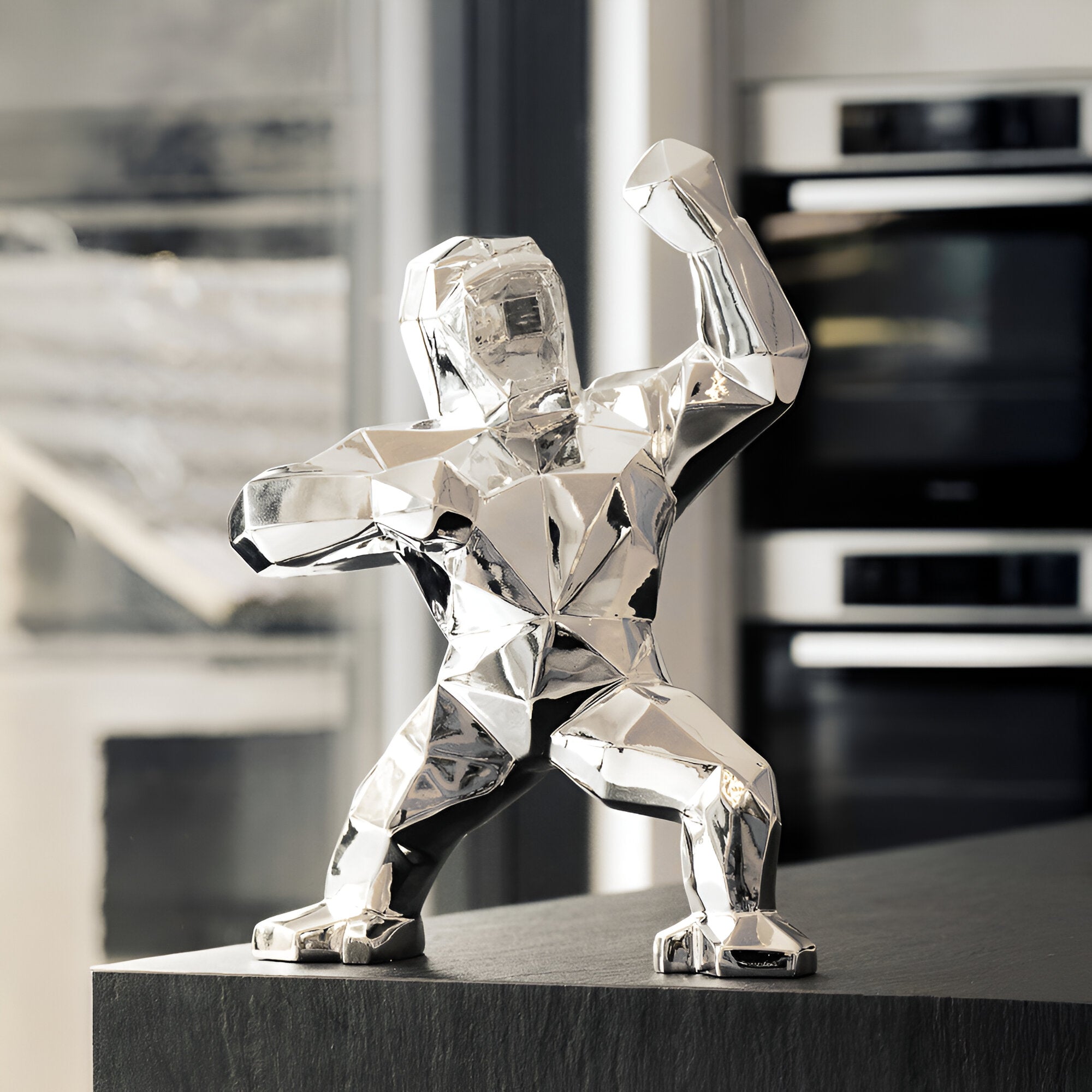 A faceted silver gorilla sculpture posed in a powerful stance on a dark countertop, with a modern kitchen setting in the background.