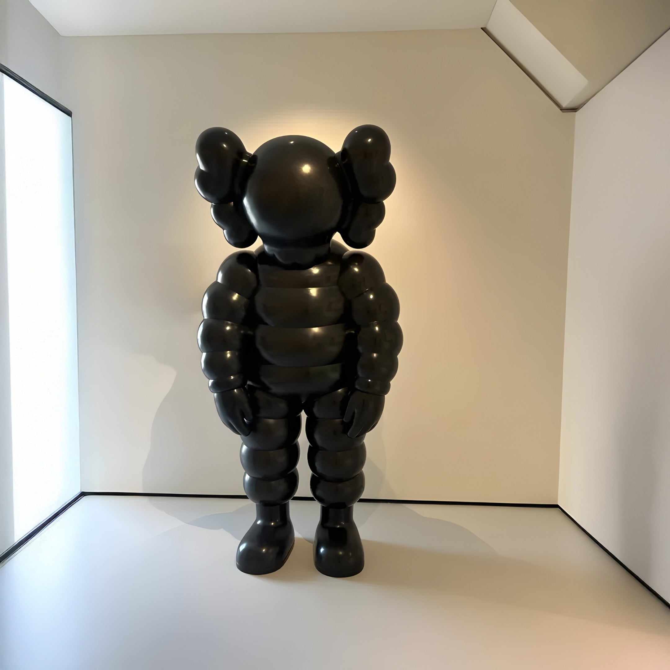 The Midnight Black Iconify Rollo Sculpture (130cm) by Giant Sculptures stands in a minimalistic, well-lit room. The cartoonish figure has exaggerated limbs, round shapes, large rounded ears, and a smooth face. The white walls and floor enhance the contemporary designs prominence.