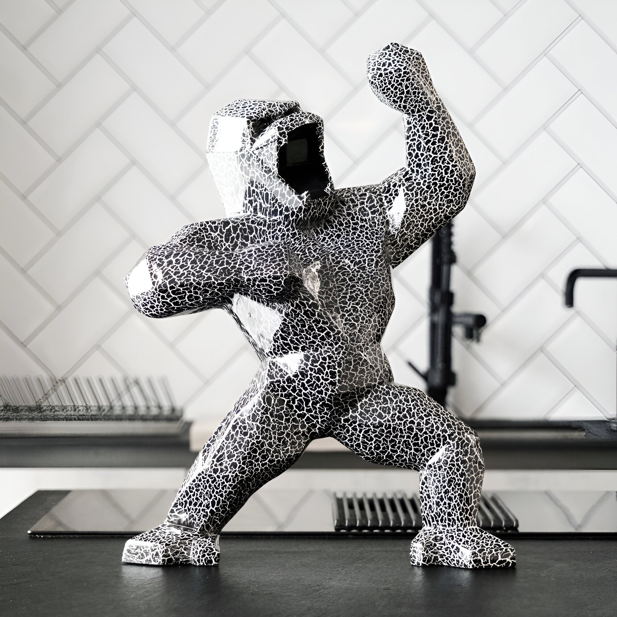 Close-up of a faceted black and white textured gorilla sculpture with a cracked pattern, displayed on a kitchen counter with a patterned tile backsplash.