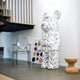 A contemporary interior space features the eye-catching Indigo Infinity Bear Sculpture - 165cm by Giant Sculptures, designed with a marble pattern. The sculpture is paired with a clear chair and a cork stool for seating. In the background, an abstract artwork presents vibrant geometric shapes, and on the left side of the room, you can partially see a wooden staircase.