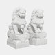 Two exquisitely detailed Chinese Guardian Lion IV Marble Outdoor Sculptures, crafted by Giant Sculptures, are placed side by side. Each lion sits majestically on an ornate base, with one paw poised on a sphere against a plain backdrop.