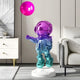 A 110cm Vibrant Gradient Astronaut Balloon Sculpture by Giant Sculptures, featuring shiny purple and teal hues, stands in a modern living room alongside a white sideboard, monochrome artwork, and a beige couch.