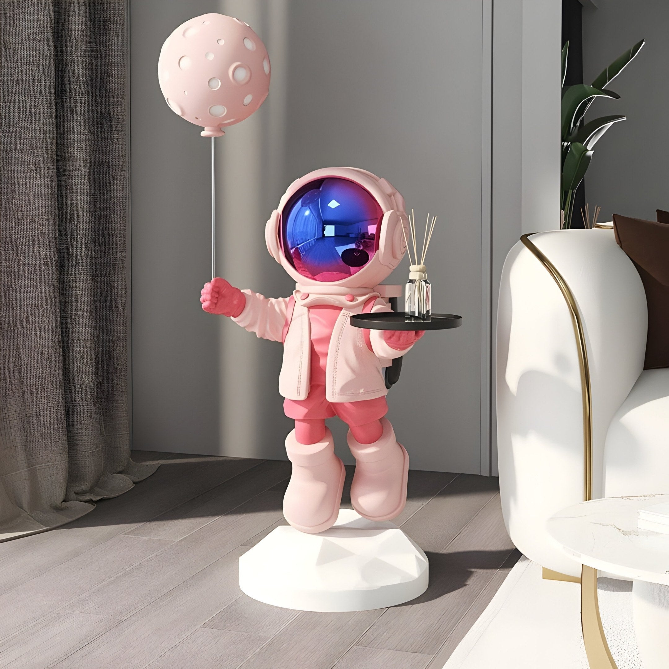 The Stellar Pink Astronaut Butler Balloon Sculpture by Giant Sculptures stands 110cm tall, elegantly holding a pink balloon and tray with a bottle and sticks on a white base, adding cosmic flair to the modern room beside the curtain and white couch with gold trim.