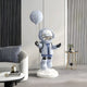 The Cosmic Sky Astronaut Moon Balloon Sculpture - 110cm by Giant Sculptures decorates a modern room featuring a sofa with cushions, a side table, and striped wall panels.