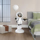 The room includes a Nova White Astronaut Butler Balloon Sculpture (110cm) by Giant Sculptures, standing beside the bed holding a tray and moon-shaped balloon, complemented by green cushions on the neatly made bed, a pouf with a leather strap, and a tall window with grid pattern.