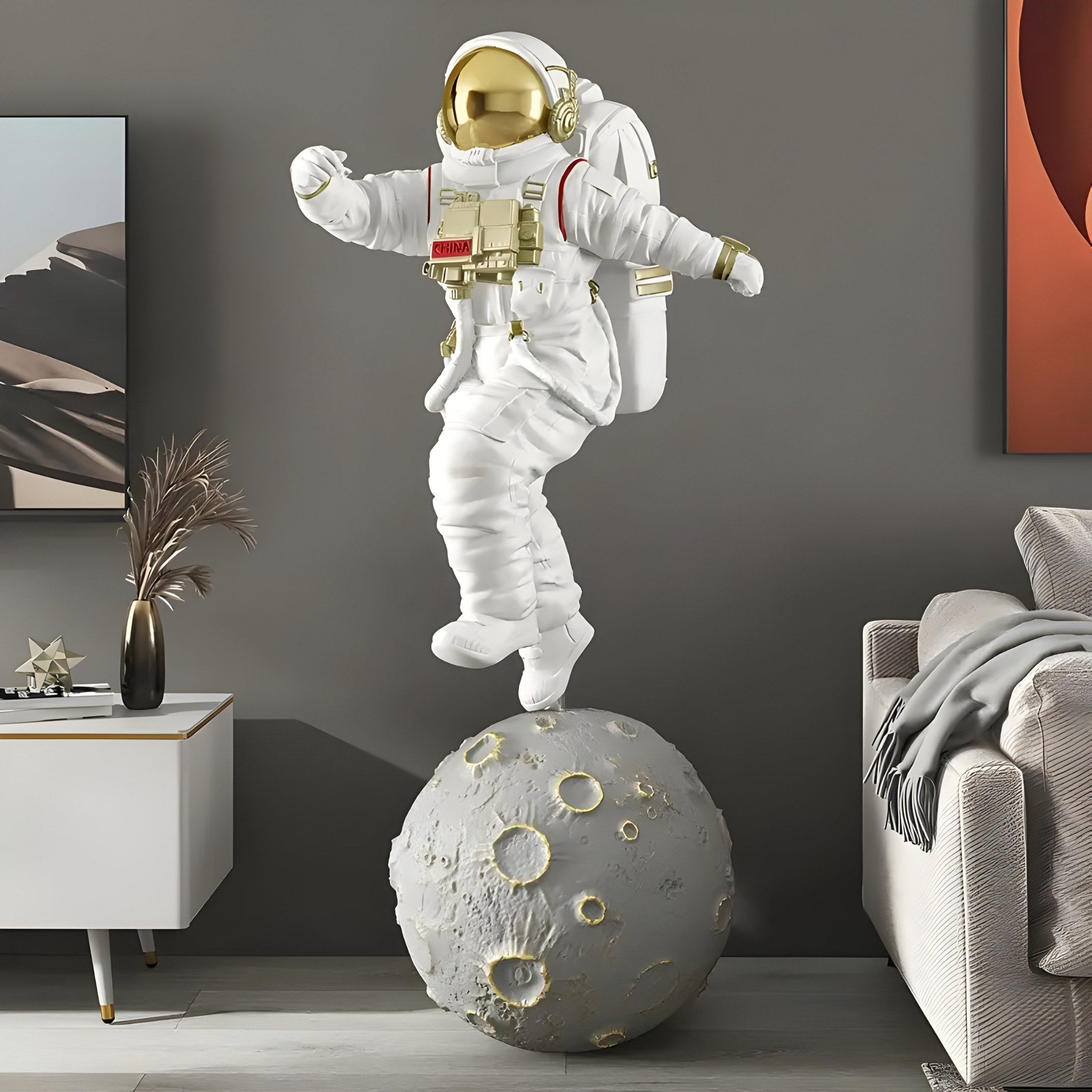 The White Space Astronaut Moon Strider Sculpture - 123cm by Giant Sculptures, features a gold-helmeted astronaut in a white suit elegantly balancing on a small moon, ideal for space-themed decor in modern living rooms with couches, side tables, and abstract wall art.