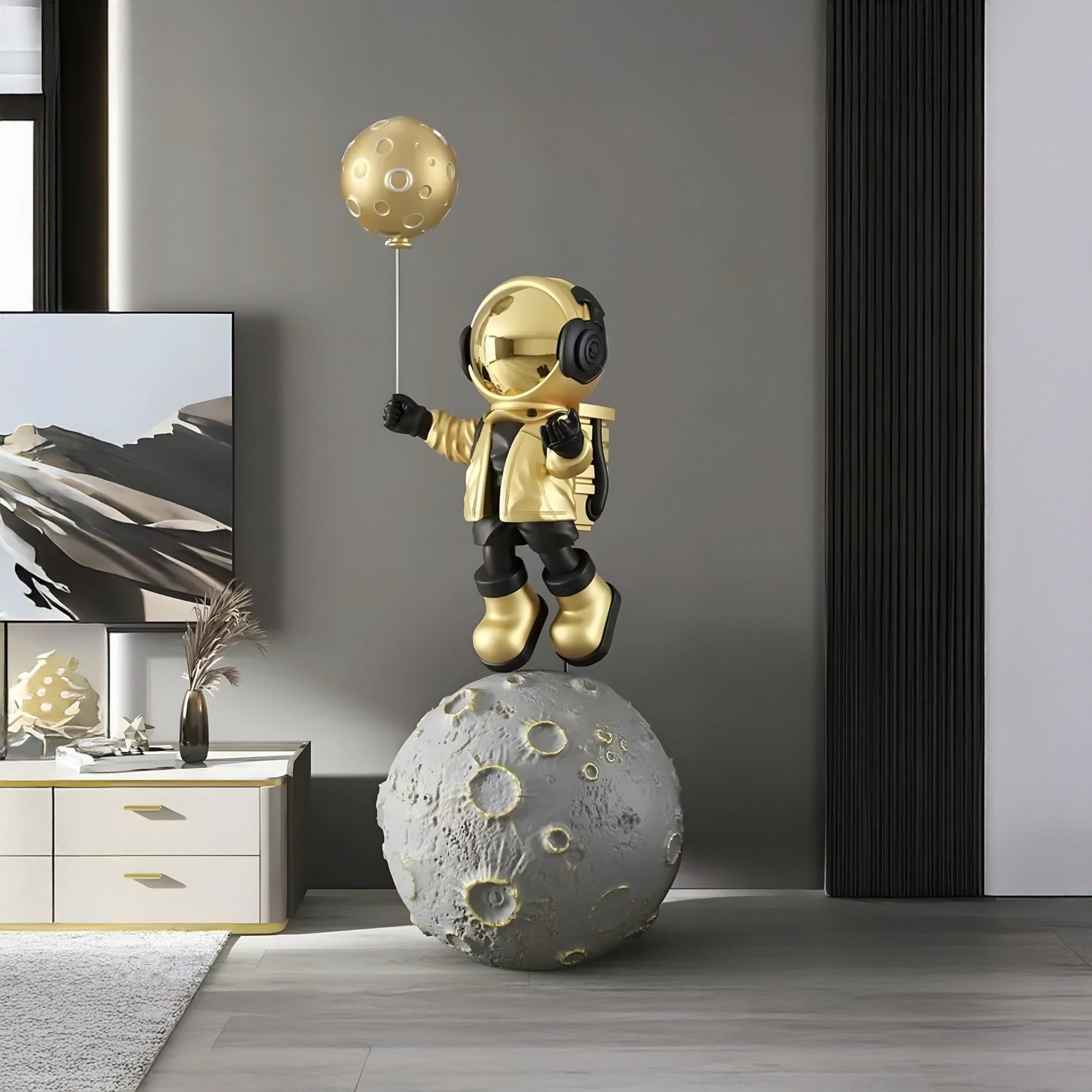 The Celestial Gold Astronaut Balloon Moonwalk Sculpture by Giant Sculptures, standing at 140cm, features an astronaut on a moon-like sphere with a textured balloon, adding modern elegance to any room with its muted tones and abstract art complementing the sleek design.