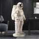 The Cloud White Space Astronaut Standing Sculpture by Giant Sculptures is the rooms cosmic centerpiece, featuring a red-accented spacesuit and reflective visor on a circular base. It complements the modern space with surrounding contemporary furnishings, including a chair and table.