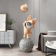 The Rose Gold Astronaut Bunny Moonwalk Balloon Sculpture (180cm) by Giant Sculptures, with its fox-like charm holding a balloon atop a moon-textured sphere, adds playful elegance to a minimalist space with white cabinets and tables.