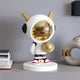 The Nova White Astronaut DJ Figure by Giant Sculptures, standing at 30cm, showcases a smooth metallic gold faceplate, gold horns, and a large gold chest orb. It rests on a round base with red and white sneakers, complementing stacked books and modern decor.