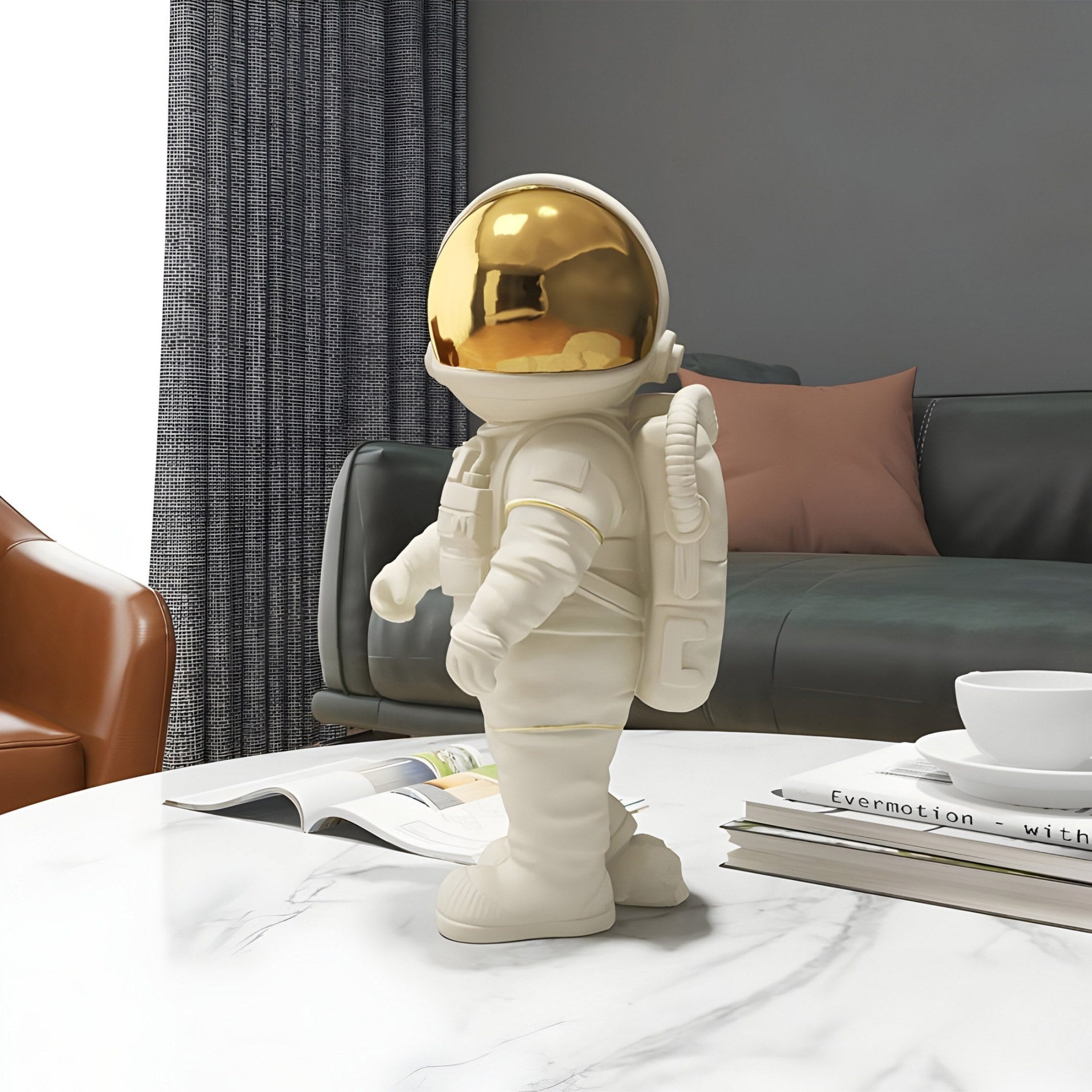 A Cloud White Stardust Astronaut Figure - 34cm from Giant Sculptures stands on a marble table with a shiny gold helmet. Behind it, theres a dark green couch with a pink pillow and a brown chair. An open magazine and white cup complete this perfect setup for space enthusiasts to enjoy.