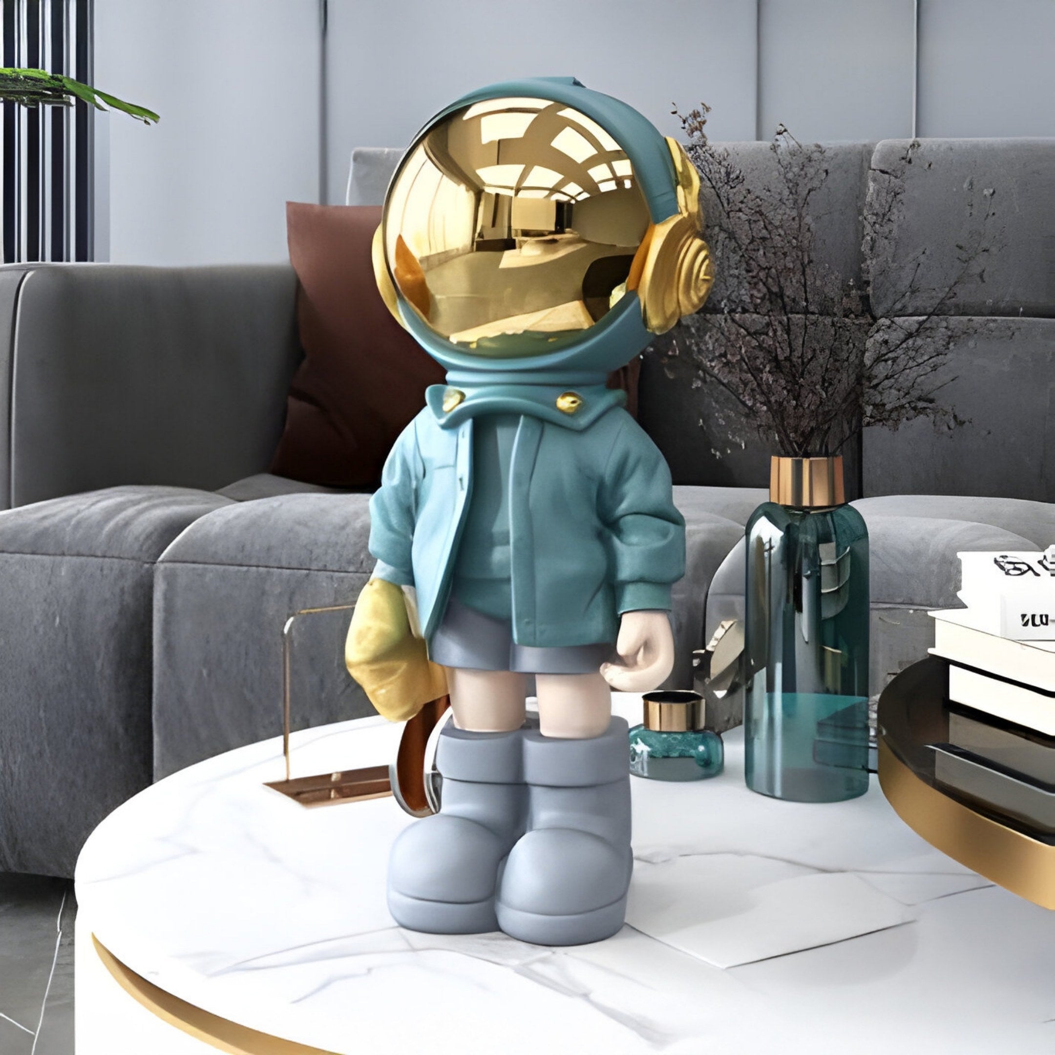 A Galactic Blue Astronaut Beats Figure by Giant Sculptures, featuring a gold helmet and teal jacket with gray boots, stands on a white marble table. A modern gray sofa, decorative plants, and a teal vase create the background.