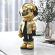 The 36cm Giant Sculptures Celestial Gold Astronaut Beats Figure, featuring a reflective visor and large headphones, stands on a glossy surface. It sports a gold jacket and boots, enhancing space-themed décor. A potted plant and sheer-curtained window complete the perfect backdrop.