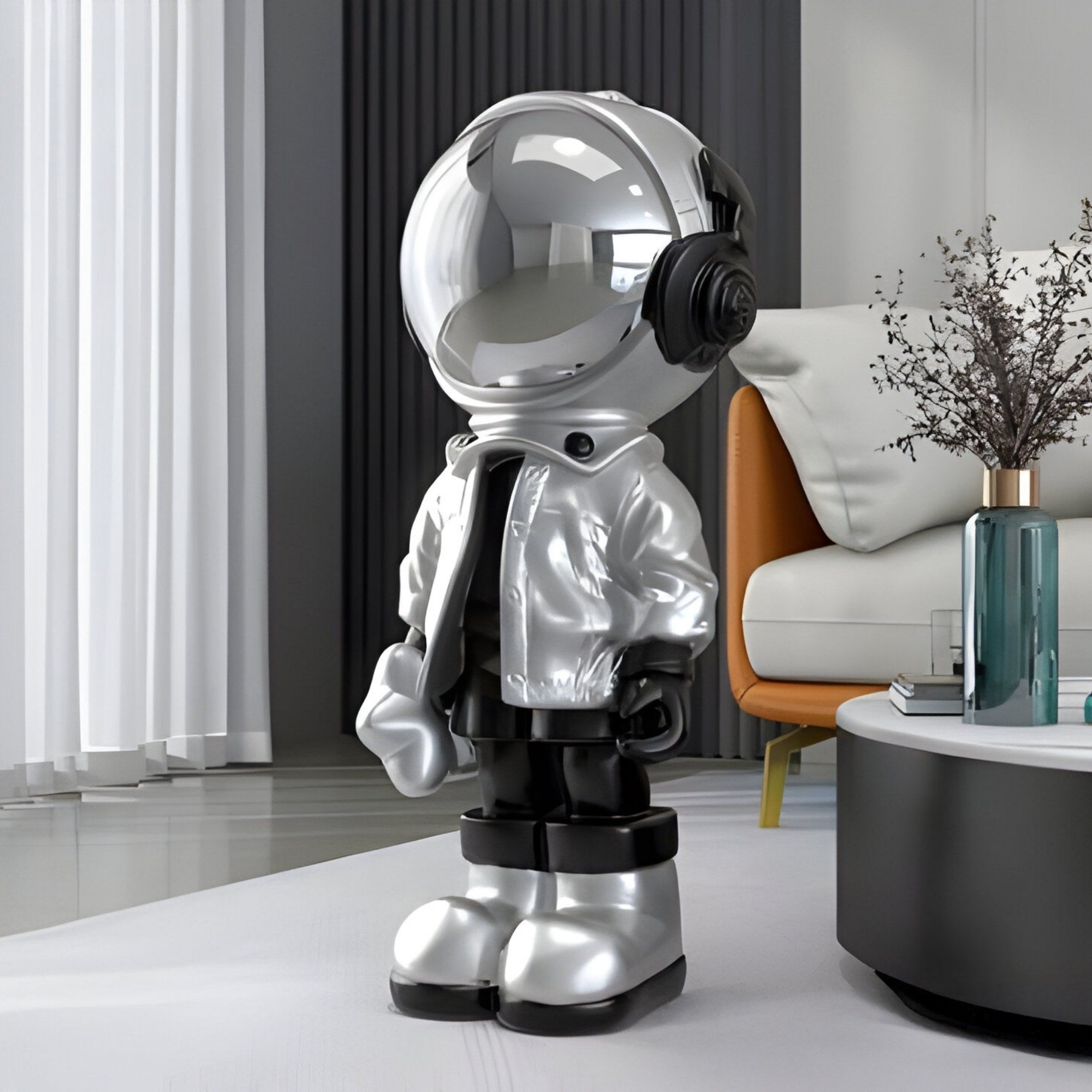 A Lunar Silver Astronaut Beats Sculpture - 70cm from Giant Sculptures stands on the floor in a modern living room. Its shiny helmet and silver jacket exude futuristic style amid white curtains, an orange chair, a sofa, and a coffee table topped with a vase.