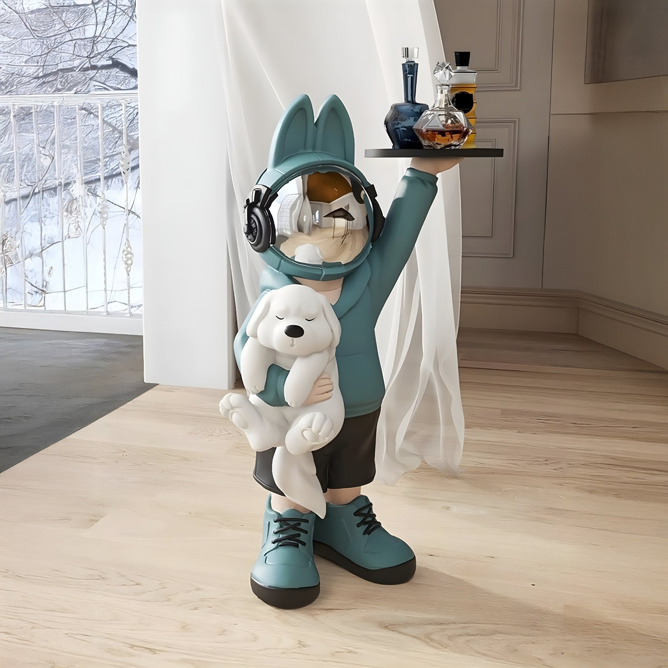 The Blue Astronaut Bunny Pup Butler Sculpture - 80cm by Giant Sculptures features a child in an astronaut helmet and teal hoodie with ears, holding a white stuffed animal and tray with bottles. Positioned indoors with a view of a snowy landscape, its ideal space-themed decor for any room.