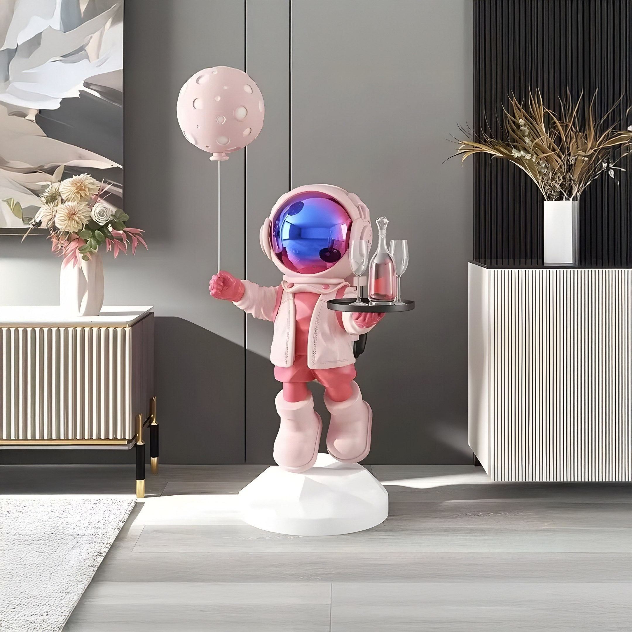 The Stellar Pink Astronaut Butler Balloon Sculpture, by Giant Sculptures, features a chic pink-suited figure with a blue visor holding a balloon and balancing wine glasses. Standing gracefully on a white pedestal, this 80cm piece adds celestial charm to modern living room decor.