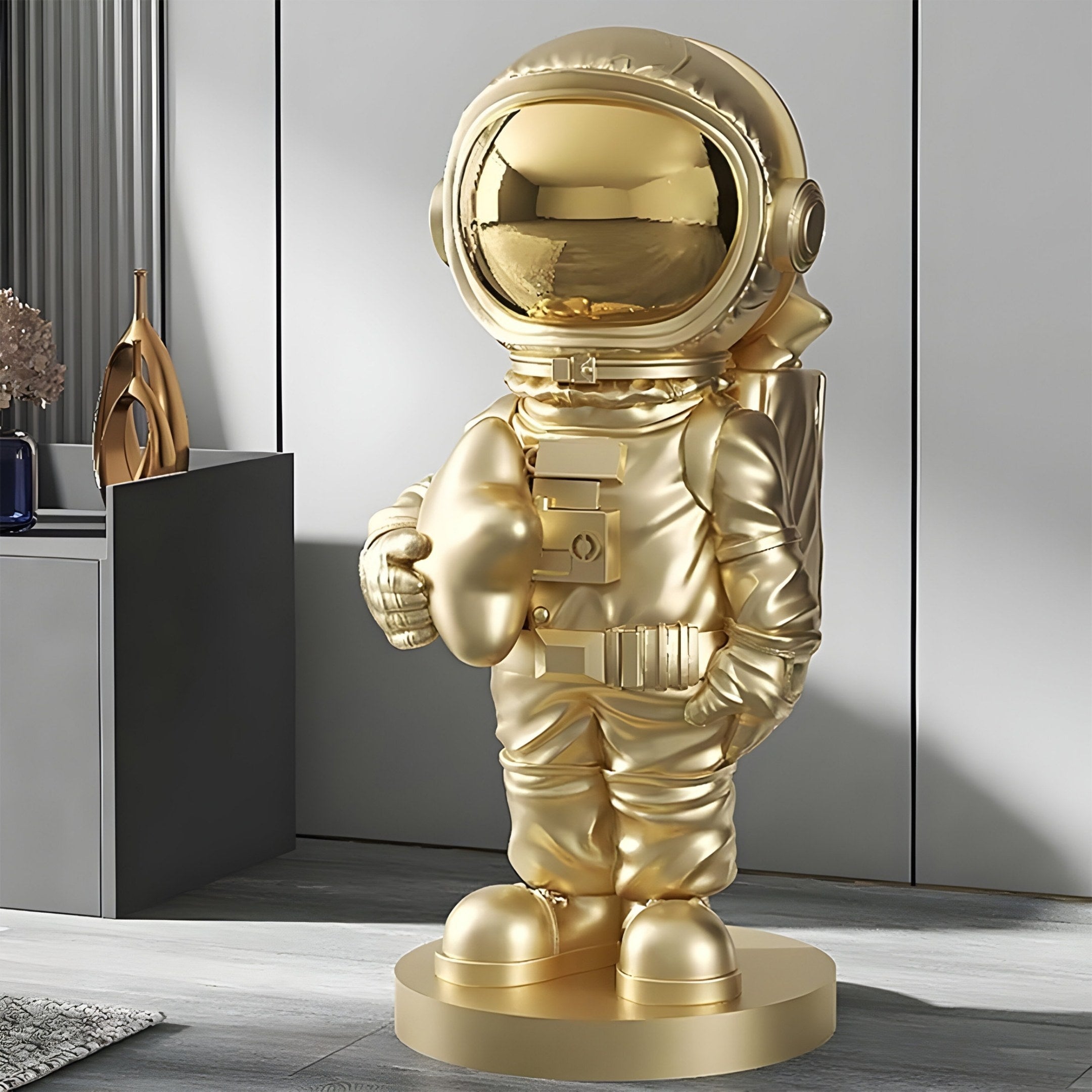 The Celestial Gold Astronaut Star Sculpture by Giant Sculptures, standing 85cm tall, graces a modern room with its glossy helmet and detailed suit. Nearby decorative vases and a textured wall complement the contemporary tribute to space exploration.