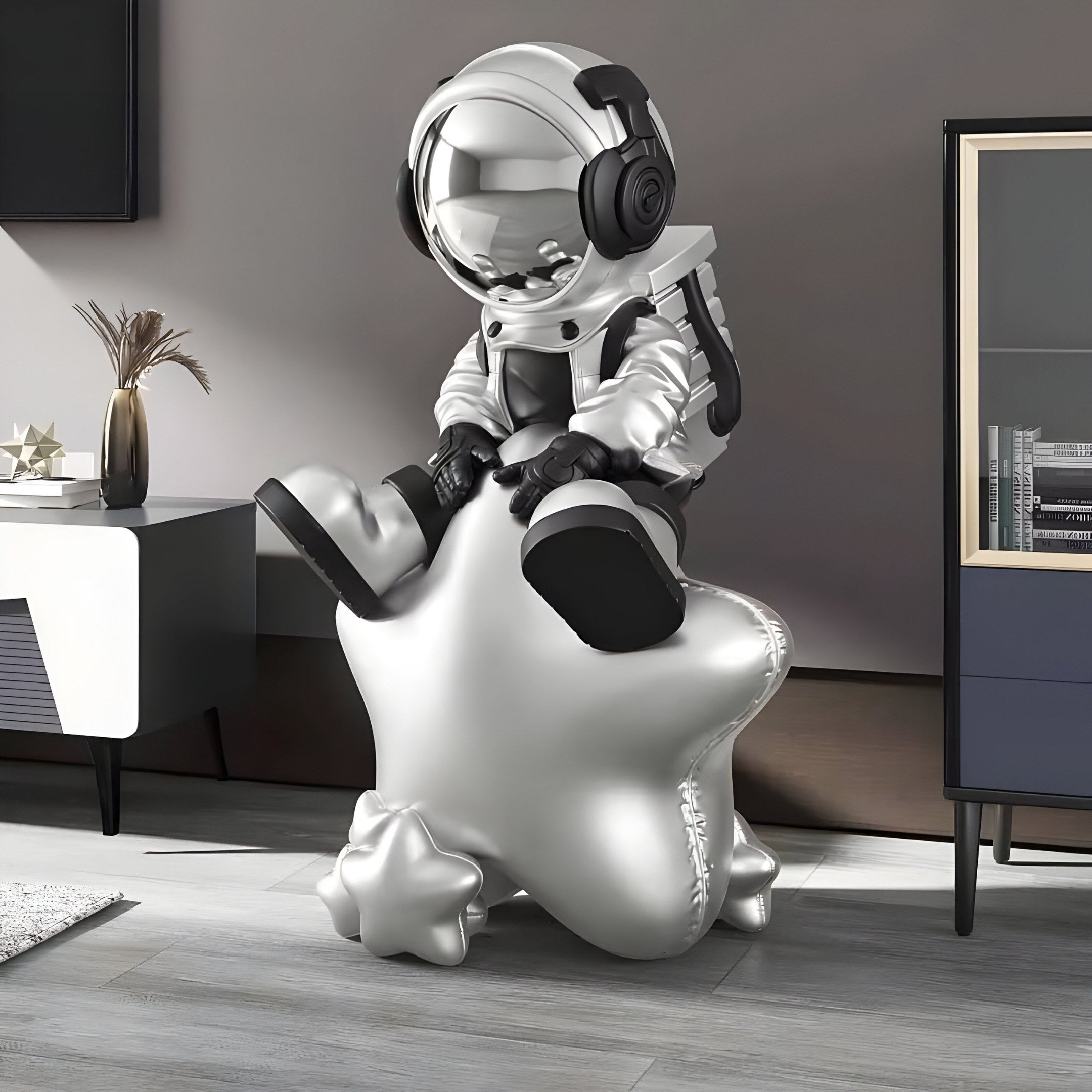 The Astral Silver Astronaut Beats On Star Sculpture by Giant Sculptures, at 90cm, features a headphone-clad astronaut on a shiny star chair, enhancing the modern rooms minimalist furniture with its reflective visor and sleek futuristic design.