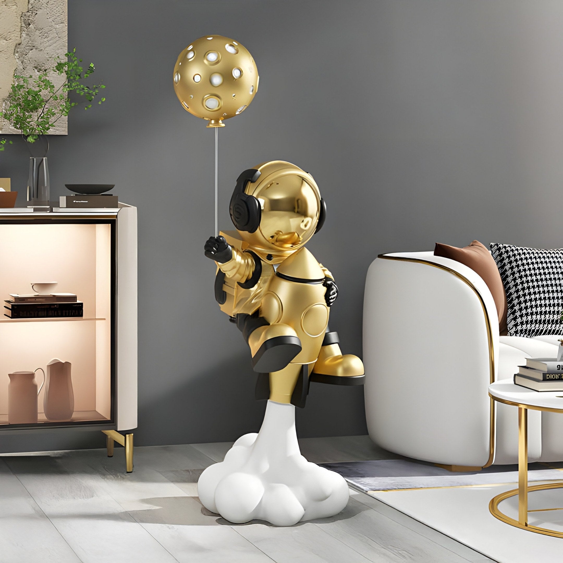 The Celestial Gold Astronaut Rocket Lift-Off Balloon Sculpture by Giant Sculptures stands on a cloud, enhancing a modern living room with its space-themed elegance, perfectly complementing the white couch, checkered pillow, and stylish cabinet.