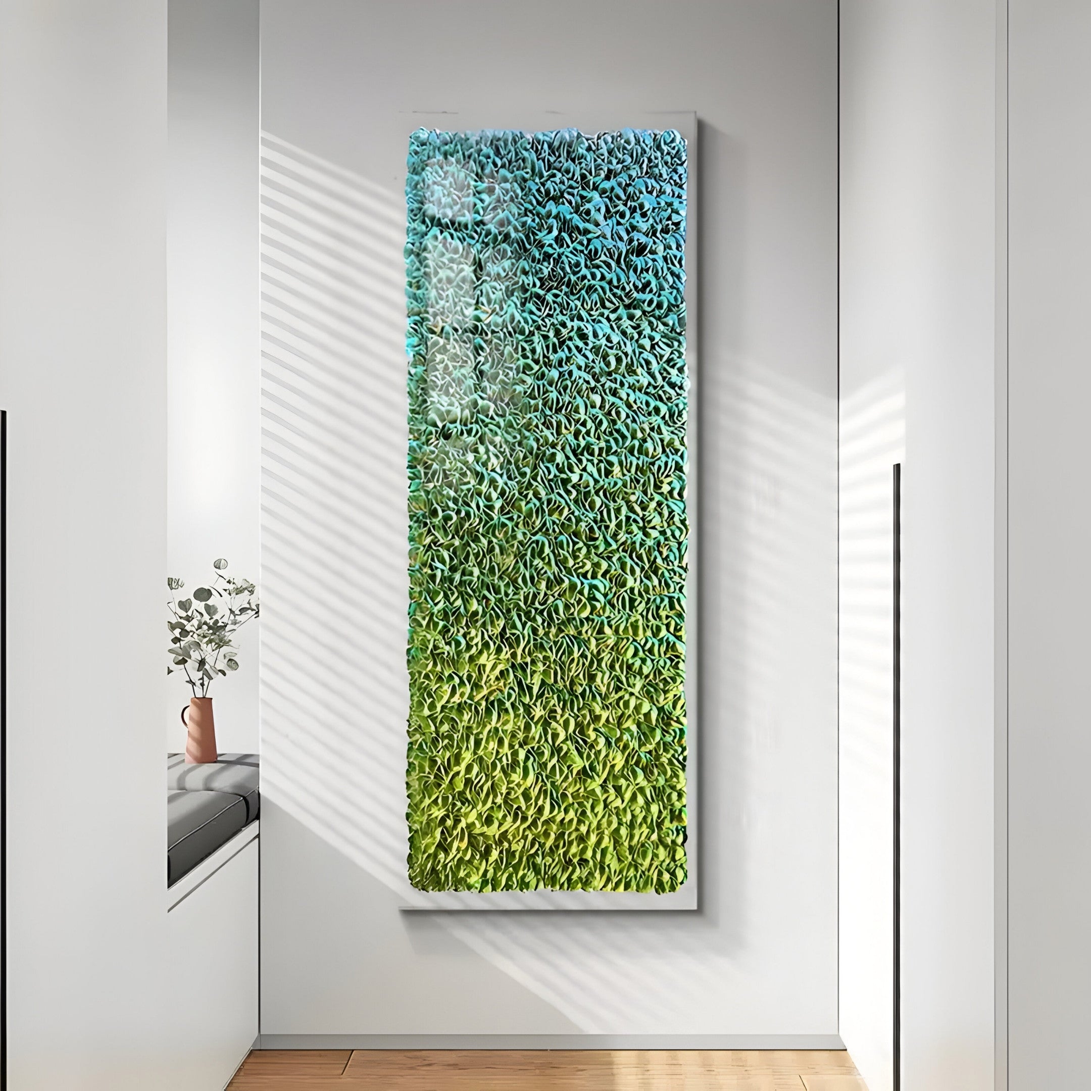 The Chromatica Rectangular Lush Green Gradient Paper 3D Wall Art by Giant Sculptures hangs on a white wall, combining textured blue and green hues. Sunlight casts shadows, while a small vase with white flowers rests on the nearby window seat.