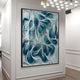 The Filigree Ocean Waves Quilling Paper Wall Art by Giant Sculptures, featuring swirling patterns of blue, teal, and white reminiscent of ocean waves, adorns a modern settings wall. Overhead lights illuminate the piece, enhancing its vibrant and dynamic appearance.