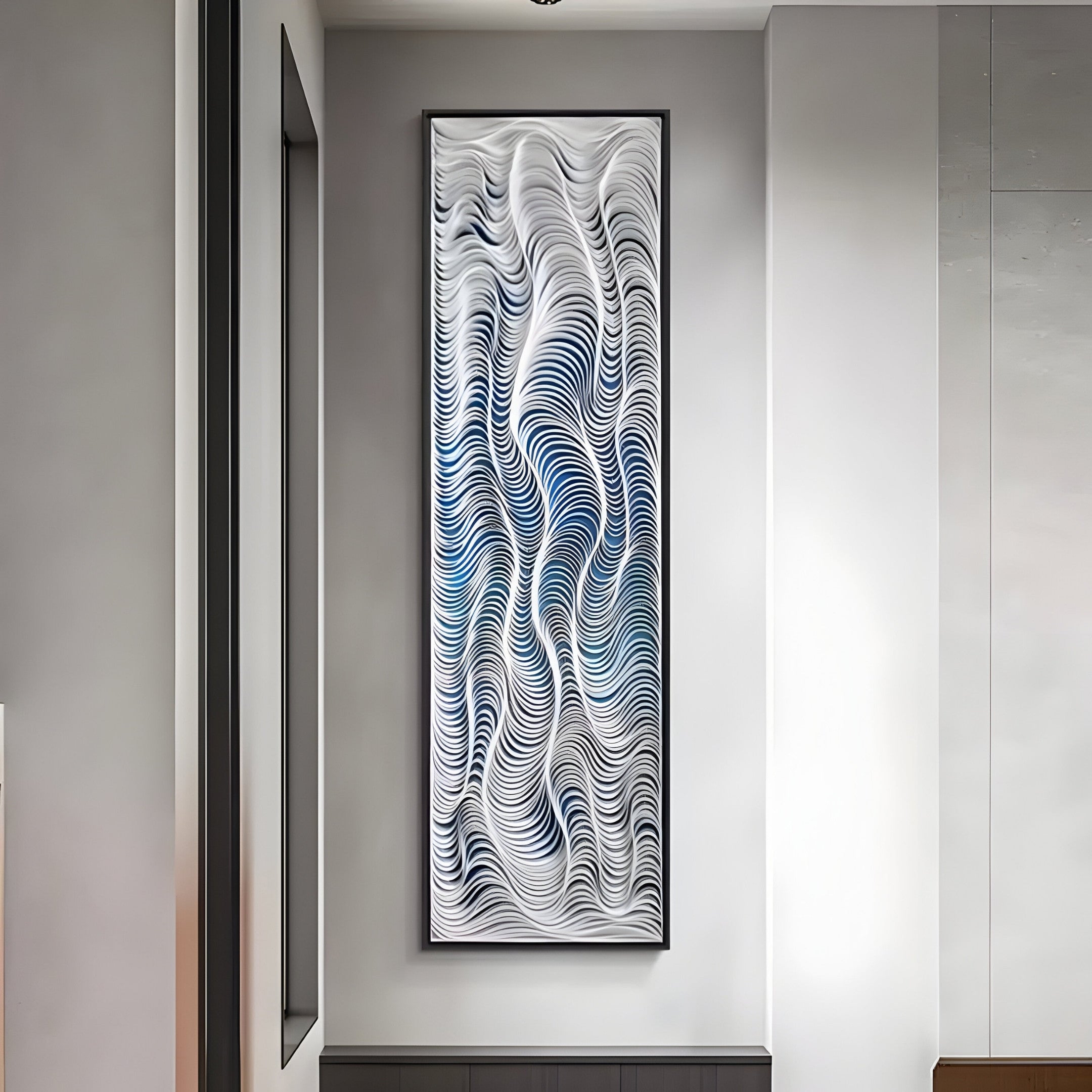 The tall Fluenta Blue Ripple Linear Cardboard 3D Wall Art by Giant Sculptures, with its wave-inspired white and blue designs, is an abstract piece. Framed on a white wall, it complements the modern minimalist room perfectly.