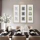 A modern dining room features a sleek black table set for four with elegant dinnerware and folded napkins. Three Lustre White Plaster Statue Vertical Decorative Wall Art pieces by Giant Sculptures enhance the minimalist vibe, while vases with white flowers and a crystal centerpiece add flair.