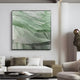 A contemporary living room features the Terrane Fresh Green Layered Abstract Wall Art by Giant Sculptures above a modern sofa, complemented by a round black coffee table and a stylish chair, creating nature-inspired elegance and minimalist decor.