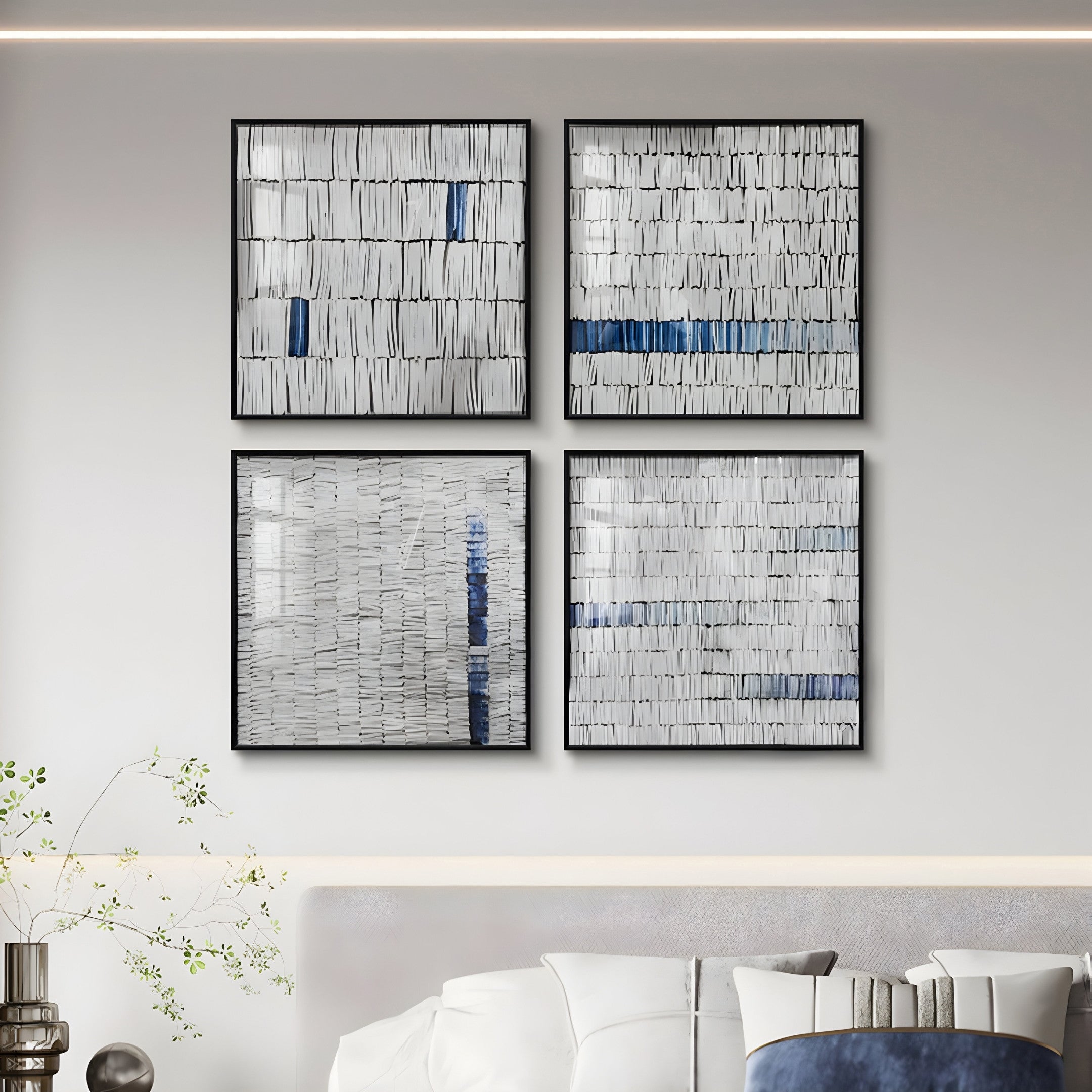 Four square abstract art pieces, titled Tracery III Blue & White Textured Paper Wall Art by Giant Sculptures, are arranged in a grid on a light wall above a modern bed. This geometric elegance enhances the contemporary interiors, with a small plant on the bedside table.