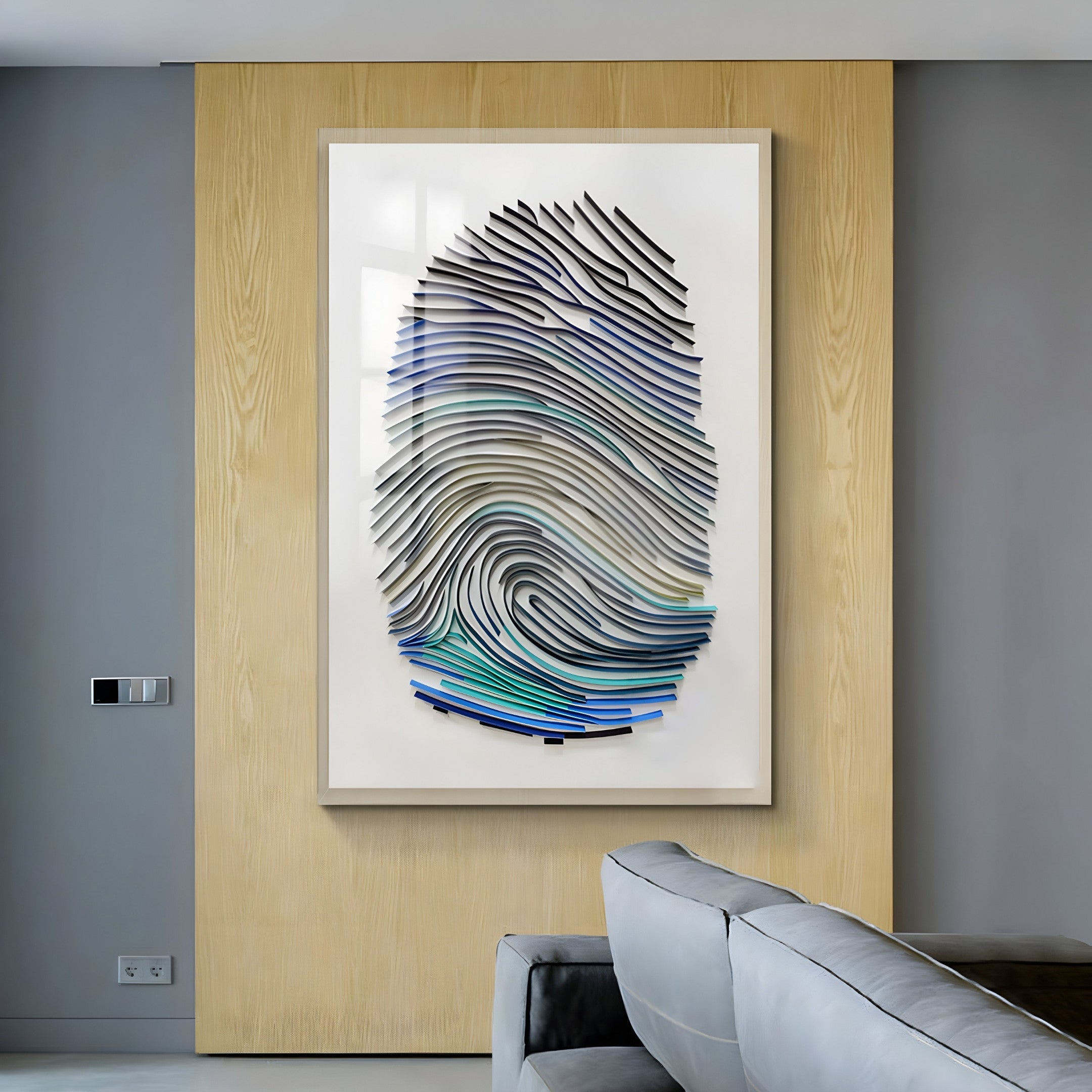 The Imprint Multi-Coloured Fingerprint Personalised Abstract Wall Art by Giant Sculptures, featuring blue, gray, and black tones on wooden paneling, serves as a centerpiece in a modern room with gray walls and a sleek gray sofa.