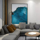 A modern living room showcases a gray sectional sofa with brown and gray cushions. A tall floor lamp illuminates the Ripplewave IV Abstract Blue Decorative Enamel Wall Art by Giant Sculptures on the wall. The look is finished with a round wooden coffee table, embodying contemporary interiors.