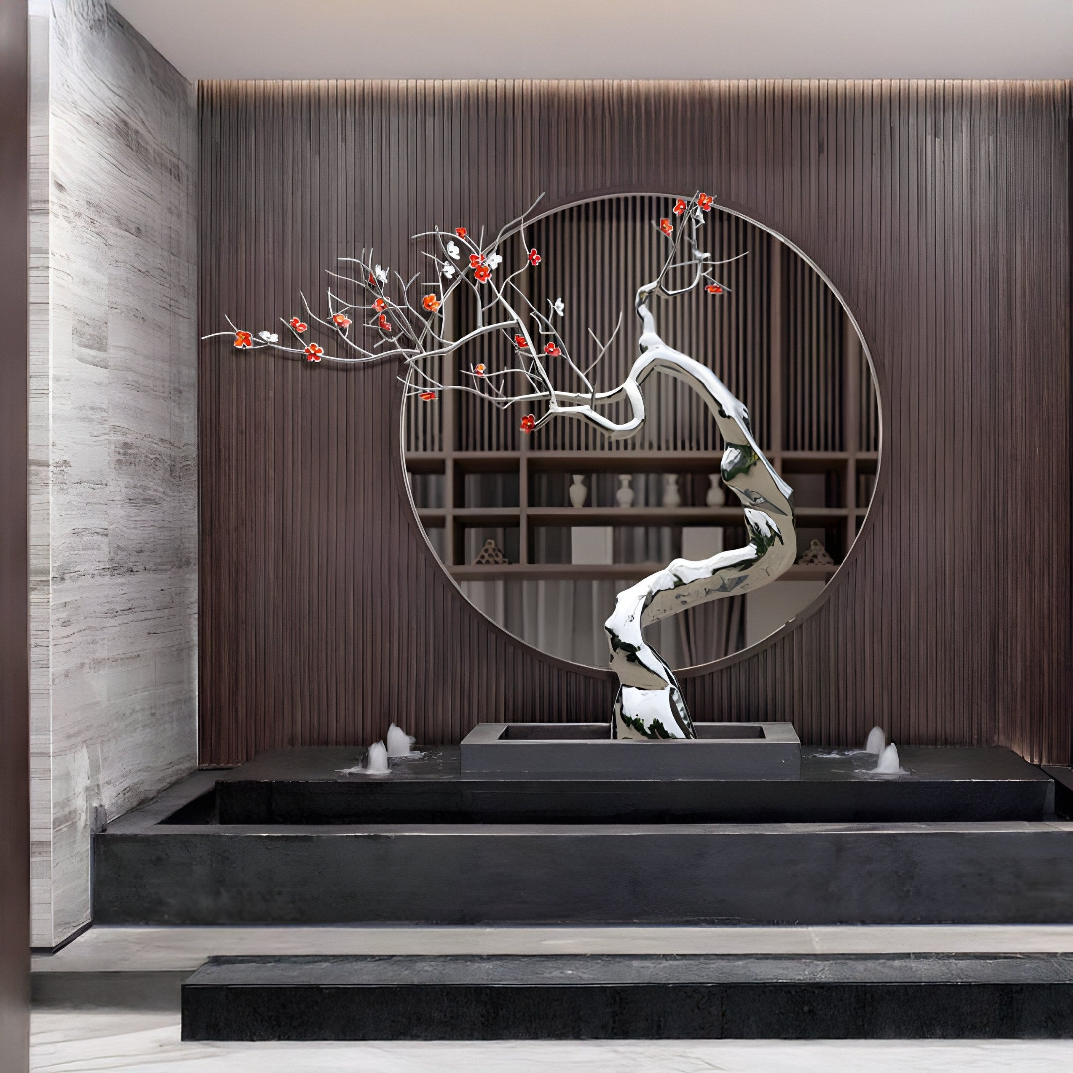 A minimalist interior displays the Blossom Tree Contemporary Steel Sculpture by Giant Sculptures, featuring small red flowers in front of a circular mirror against a wood-paneled wall. It sits on a black rectangular planter integrated into a sleek water feature, epitomizing modern artistry.