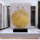 The Mesh Gold Geometric Steel Sculpture (135/200cm) by Giant Sculptures stands elegantly on a black pedestal in a modern, minimalist interior with tall white and black walls adorned with subtle lighting.