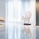 A modern minimalist room features the Cheri Copper Abstract Steel Sculpture by Giant Sculptures, standing elegantly on a glossy white floor. Sheer white curtains cover the windows, while a linear fireplace creates a soft glow in the background. Vertical black and white panels add contrast to the space.