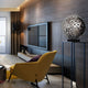 This living room embodies modern elegance with a sleek flat-screen TV on a wood-paneled wall. A yellow armchair faces the TV, and an Eclipse Silver Abstract Steel Sculpture by Giant Sculptures graces a tall stand beside a decorative lamp. Natural light flows through large curtained windows.