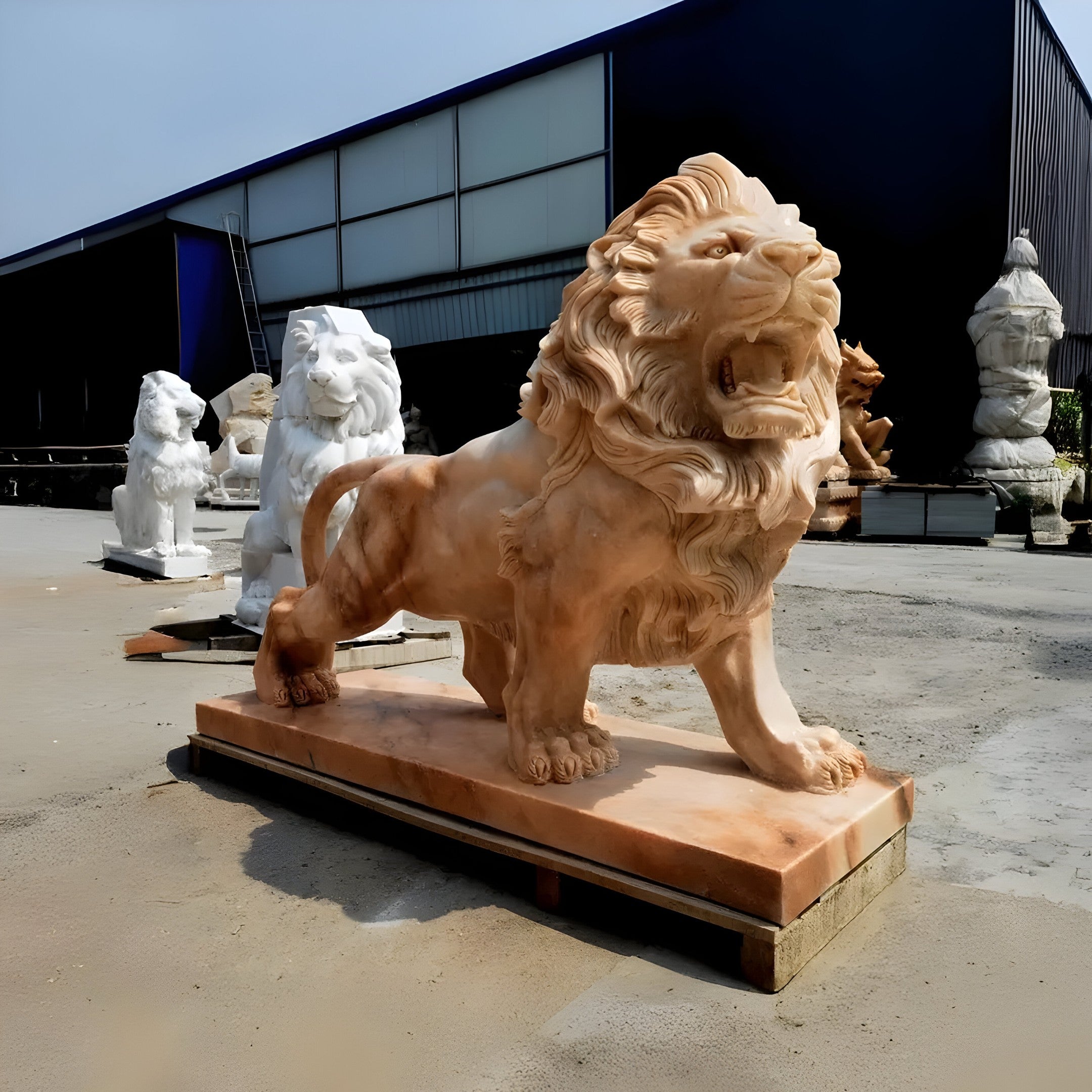 The Giant Lion II Yellow Marble Outdoor Sculpture - Customised by Giant Sculptures, featuring an intricately detailed mane, stands majestically on a wooden platform. Several other lion sculptures enhance the landscape outside a large dark blue building. This luxury outdoor décor crafts an impressive scene under clear skies.