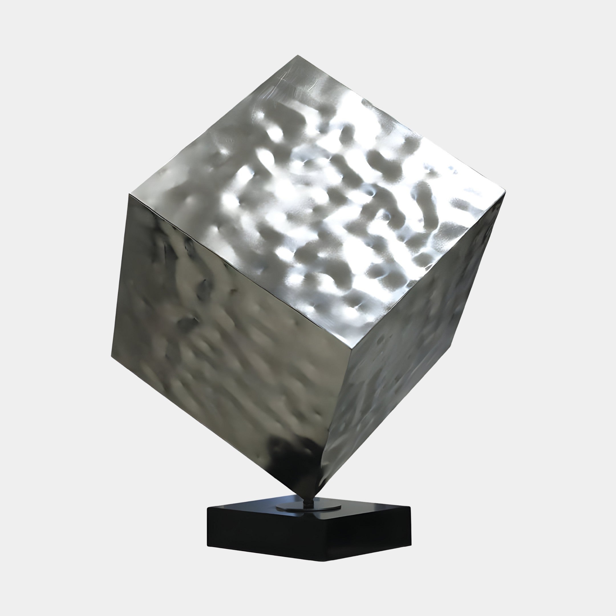 Silver cube-like sculpture with a wavy surface, displayed at an angle on a black base.