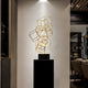 Tall gold wireframe cube sculpture styled in a modern art gallery setting, standing on a black pedestal.