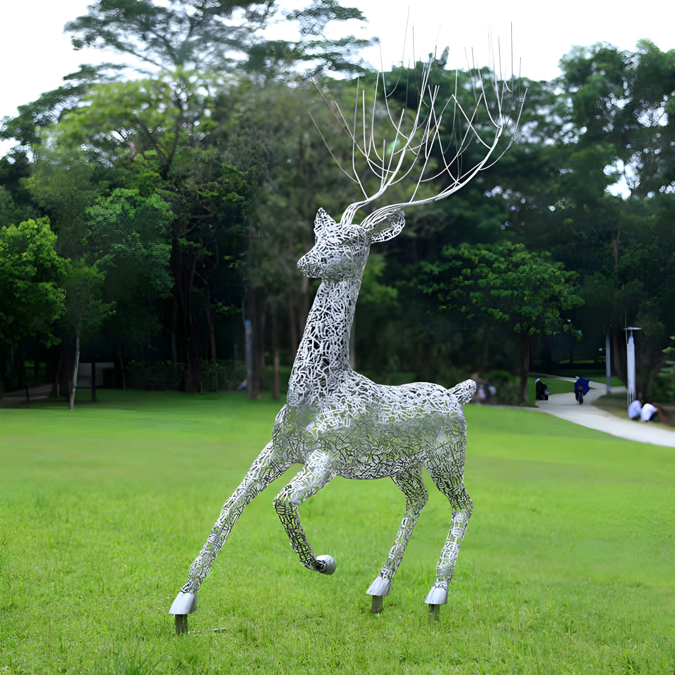 The Arcane Stag Steel Outdoor Sculpture by Giant Sculptures, standing at 205cm, is crafted in stainless steel with intricate wire patterns. Its elongated, abstract antlers create a whimsical feel amidst the grassy field and trees, with pathways and seated park-goers enhancing the serene atmosphere.