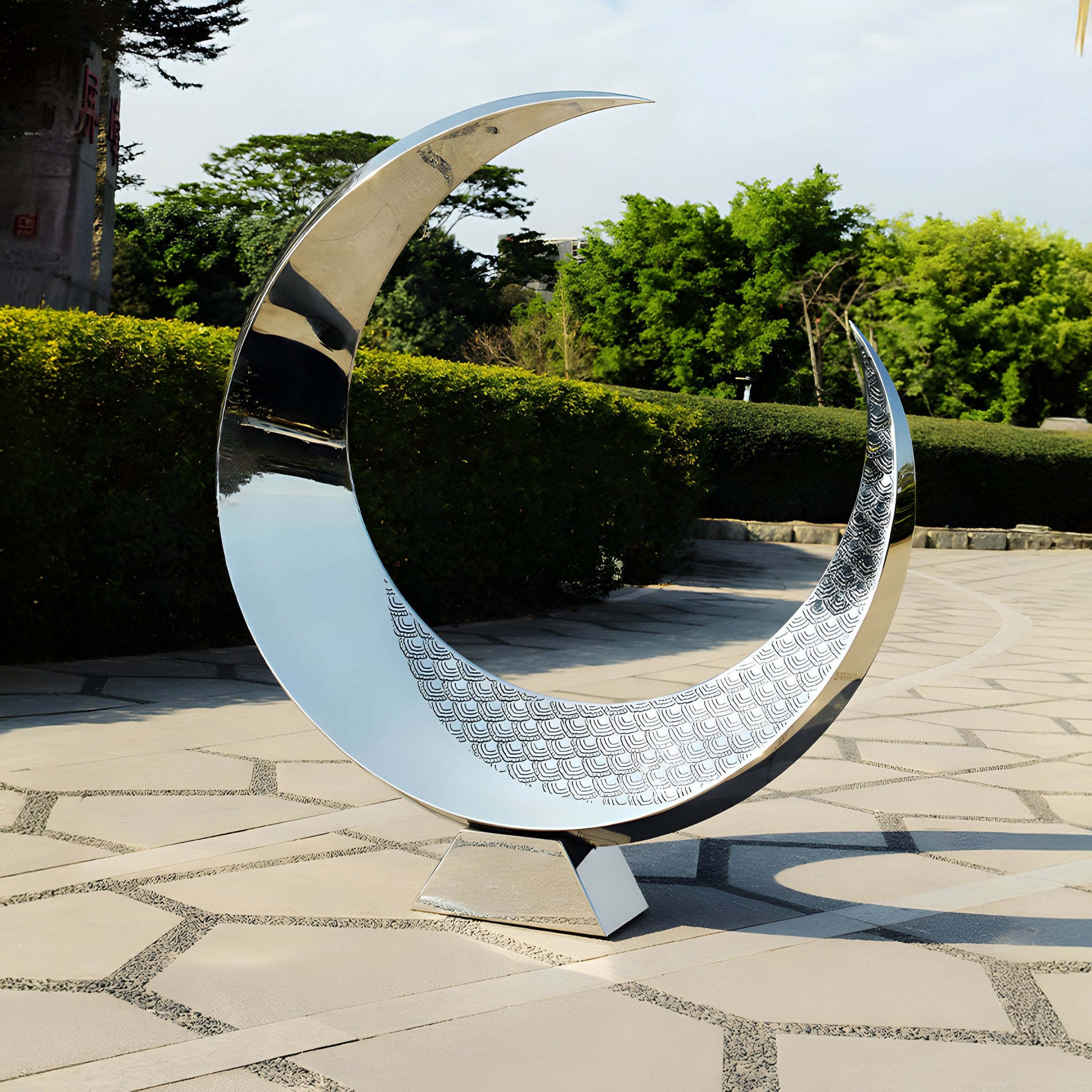 A reflective crescent stainless steel sculpture placed in a serene outdoor garden setting, reflecting its surroundings with a tranquil, modern appeal.