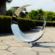 A reflective crescent stainless steel sculpture placed in a serene outdoor garden setting, reflecting its surroundings with a tranquil, modern appeal.