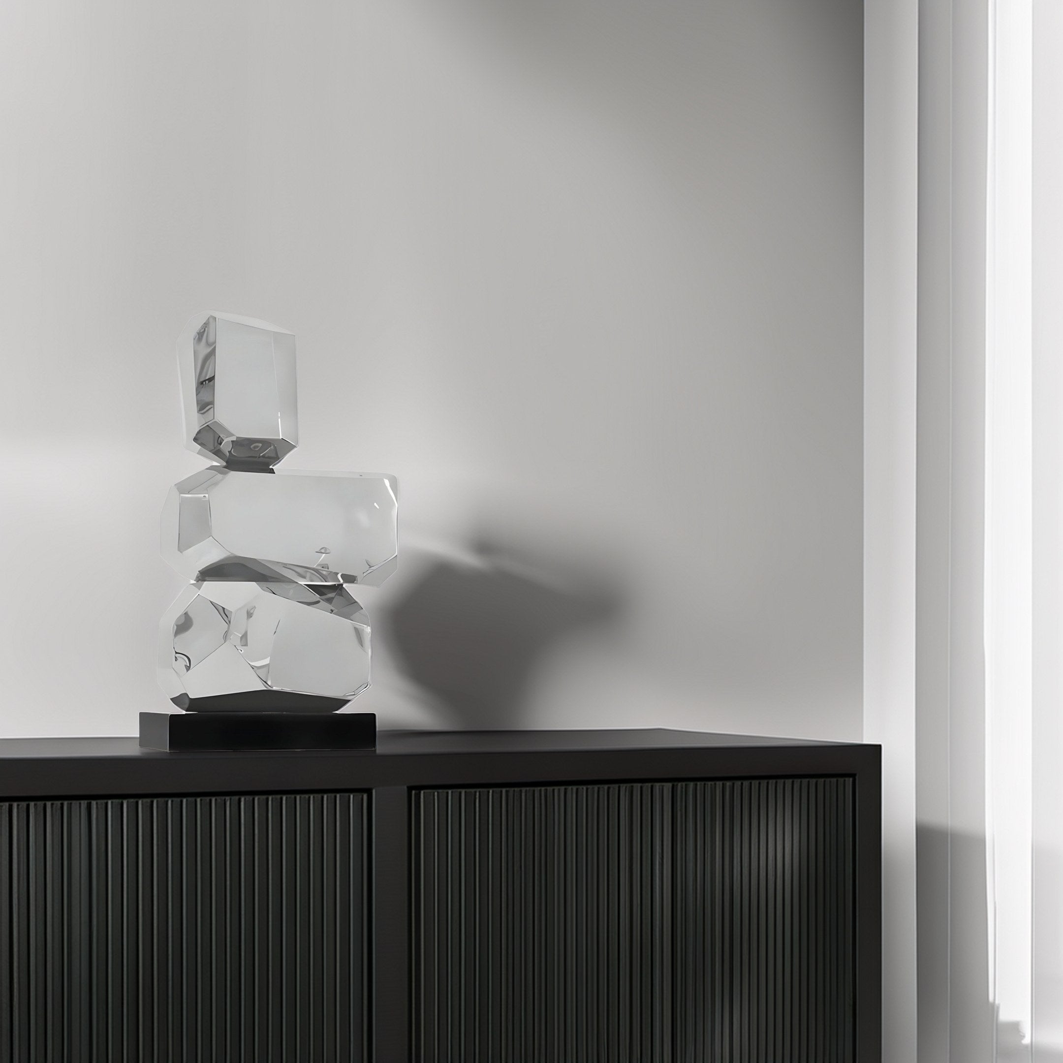 A minimalist room corner showcases the Monoform Stone II Steel Sculpture - 73cm by Giant Sculptures on a dark cabinet. Set against a soft gray wall with partially visible white curtains, the room exudes timeless elegance and a modern, sophisticated aesthetic.