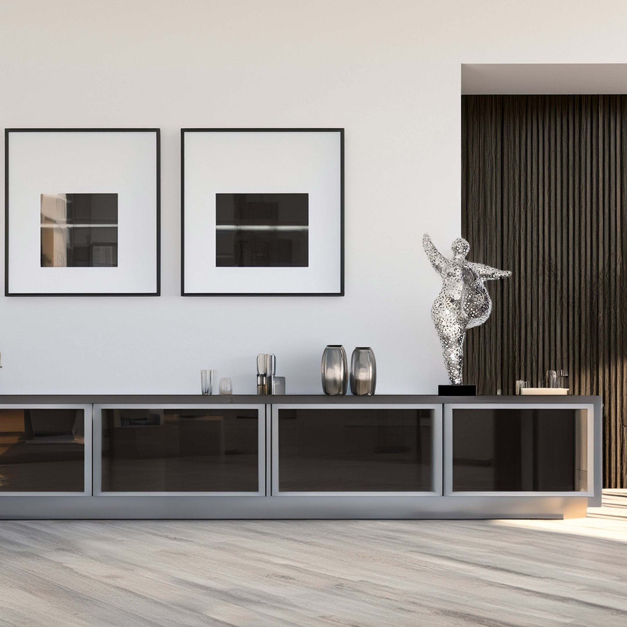 A modern living room with a sleek console table with glass doors, two abstract artworks above, and Giant Sculptures Nimbus Silver Organic Steel Sculpture - 95cm. The room has light wood flooring and a textured dark wall panel.