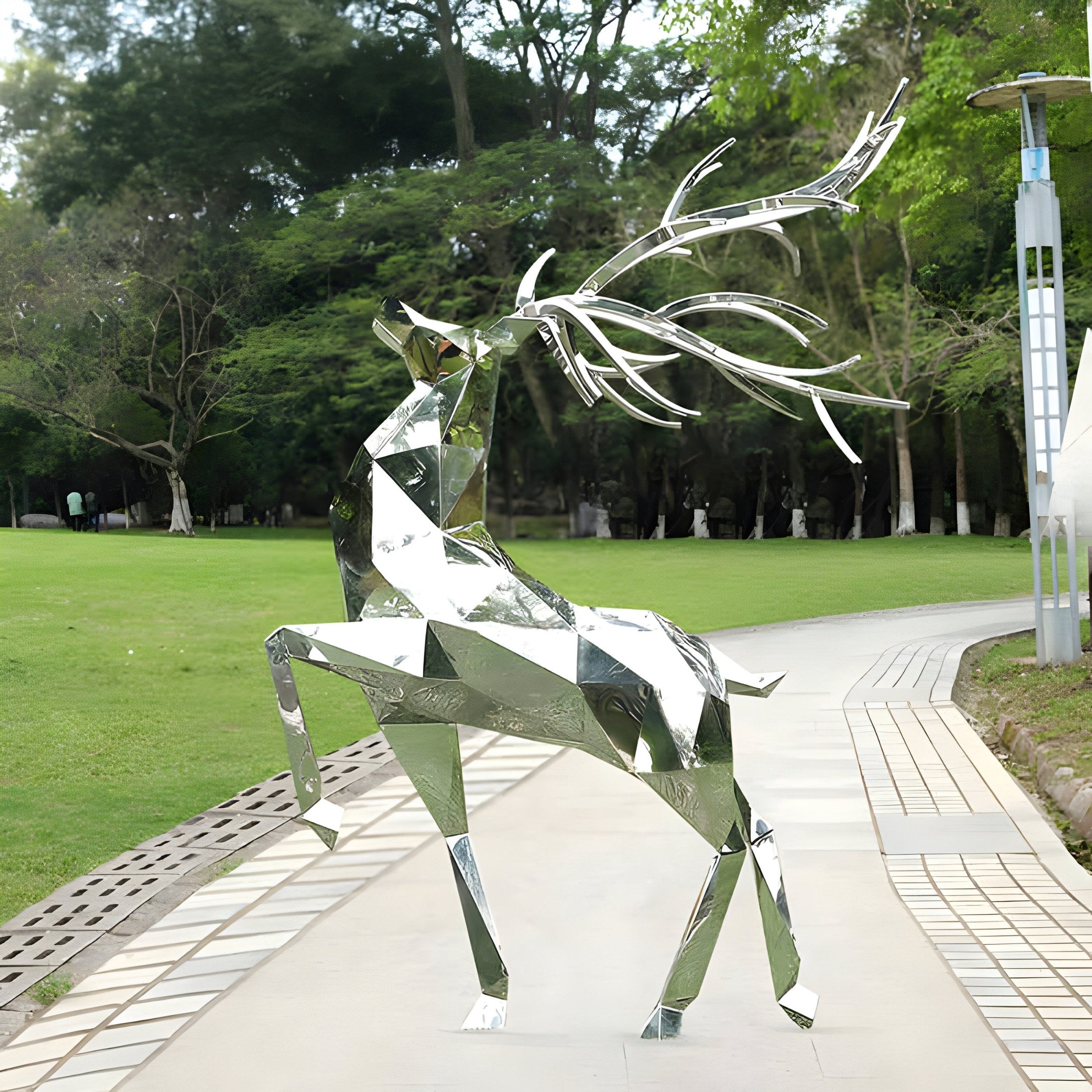 The Noble Deer II Geometric Steel Sculpture by Giant Sculptures, standing at 198cm, is a modern outdoor art piece. Made of stainless steel, it beautifully reflects green surroundings and graces the park pathway with its striking geometric design and large antlers.